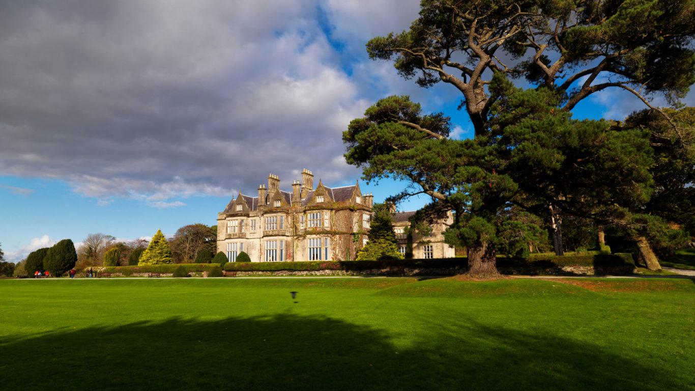 Grand historical hotel with lush grounds and towering trees, offering serene views and elegant architecture under a vast sky.