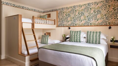 Family-friendly hotel room with a king bed, bunk beds, floral wallpaper, green accents, and a cosy atmosphere.