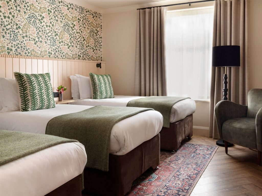 Spacious room with three cosy beds, floral wallpaper, elegant lamps, and comfortable seating creates a welcoming retreat.