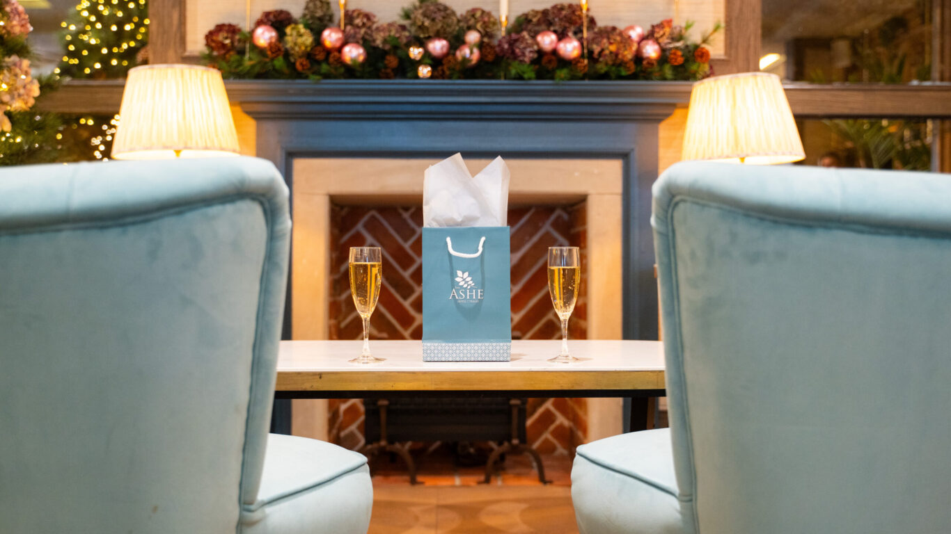 Cosy lounge with soft chairs, lit fireplace, festive decor, and champagne, perfect for a relaxing hotel experience.