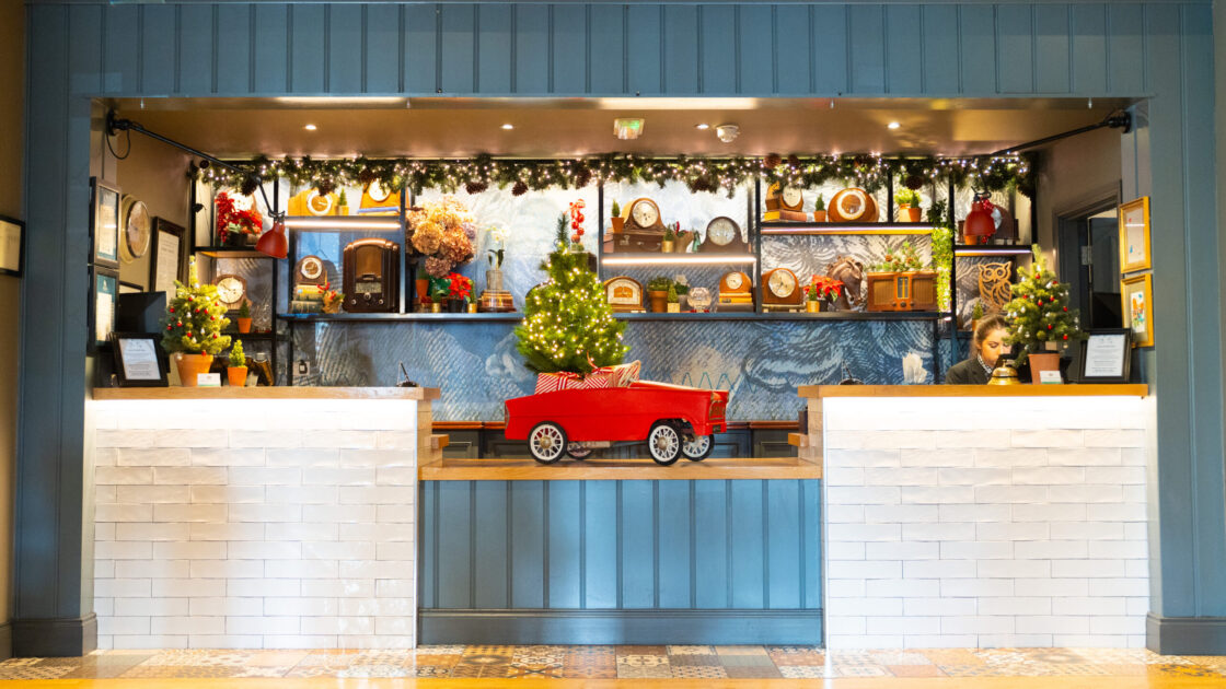 Charming hotel reception with festive decor, a mini red car display, and welcoming staff offering a warm, inviting atmosphere.