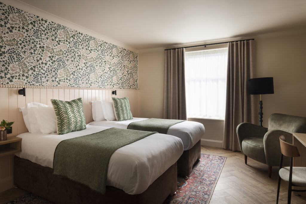 Charming twin room with floral wallpaper, cosy armchair, soft lighting, and elegant decor for a relaxing stay.