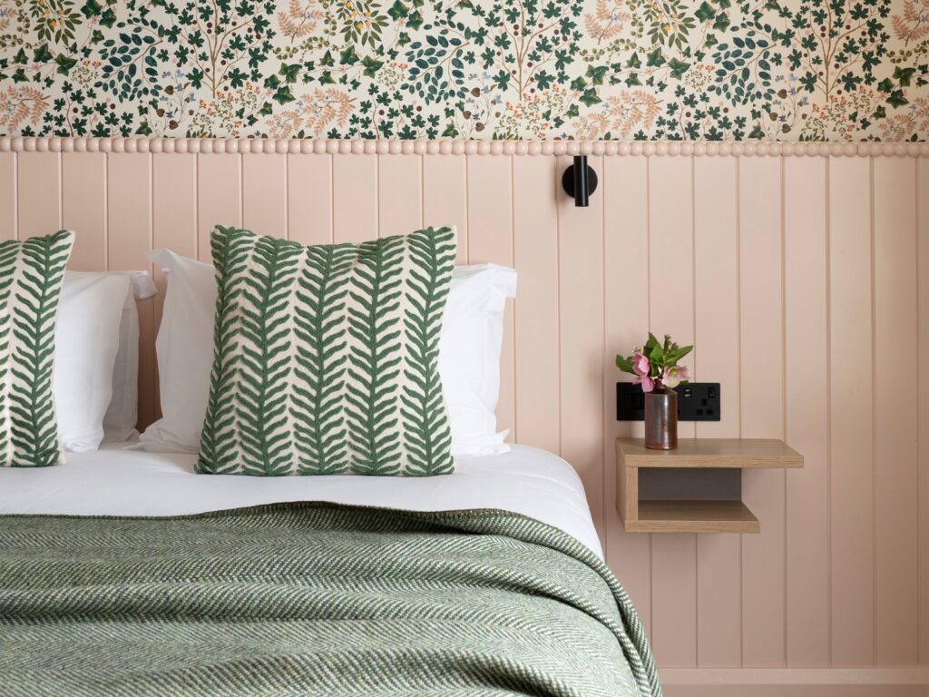Charming Hotel Room Decor Cosy hotel room with a large bed, floral wallpaper, green cushions, and a bedside shelf with fresh flowers.