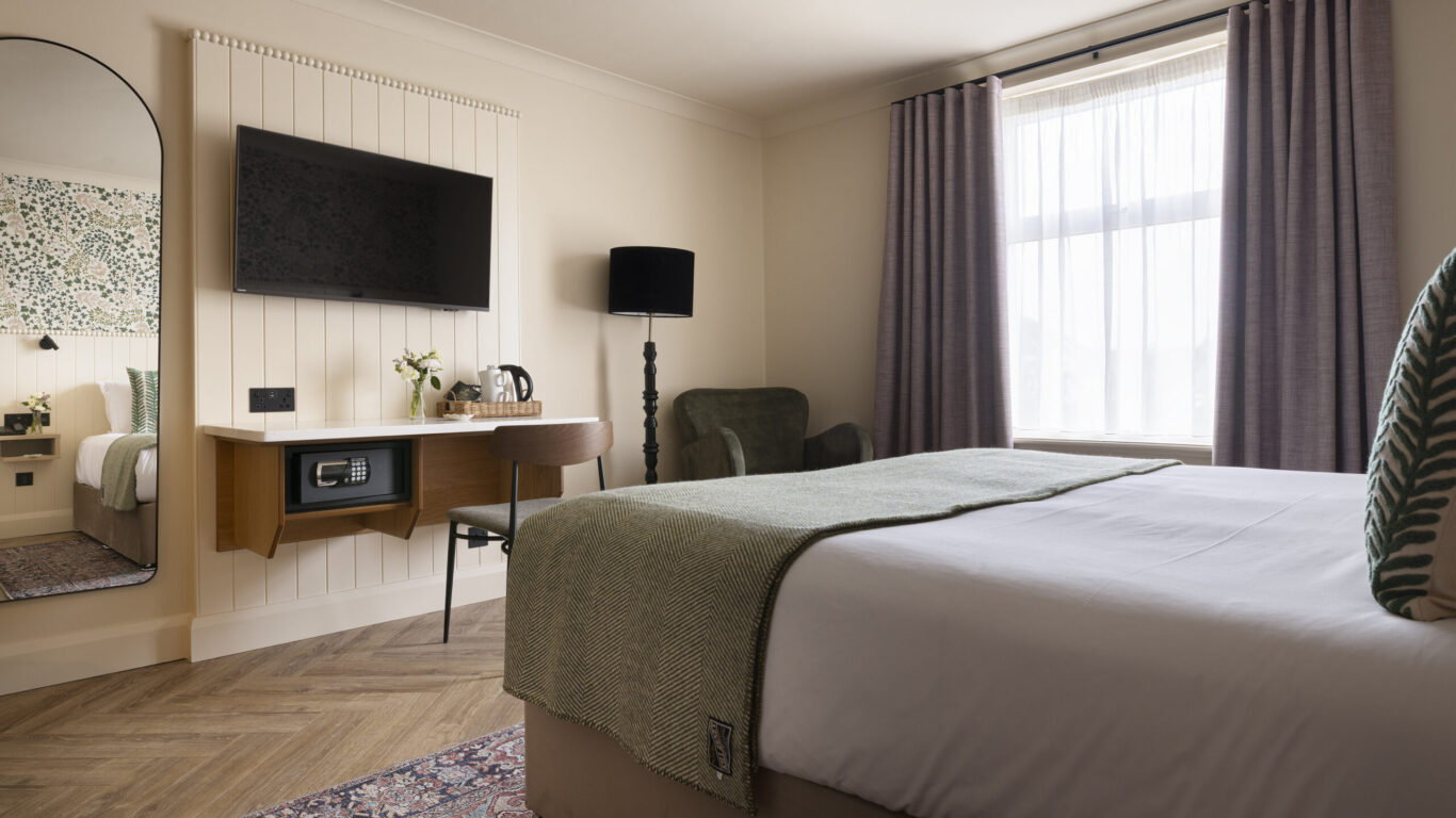 Elegant hotel room with cosy bed, wall-mounted TV, stylish decor, large window, and a welcoming vibe, perfect for relaxation.