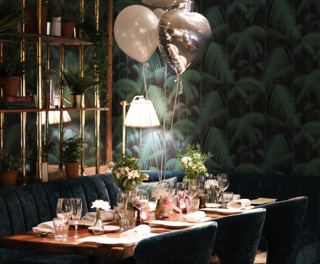 Elegant dining table set with flowers, plush seating, ambient lighting, and celebratory balloons in a luxurious hotel restaurant.