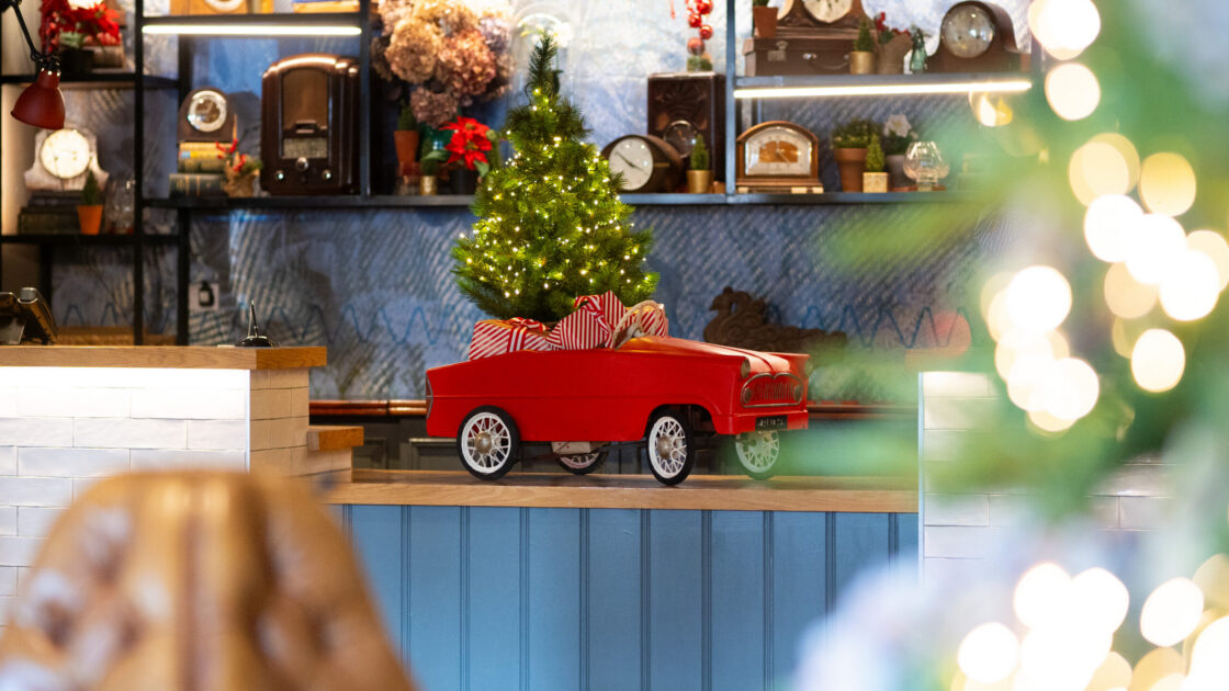 Festive red toy car with gifts and tree at charming hotel lobby. Cosy atmosphere with warm decor. Perfect holiday retreat.